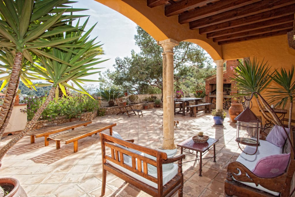 Dos bancos de madera con respaldo y una mesita al centro en el porche que es parte de una terraza hermosa en la villa