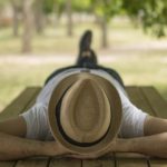 Un hombre con sombrero acostado sobre una mesa de madera descansando bajo la sombra en el jardín de la villa