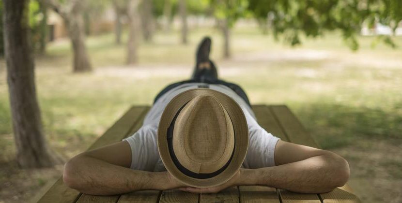 Un hombre con sombrero acostado sobre una mesa de madera descansando bajo la sombra en el jardín de la villa