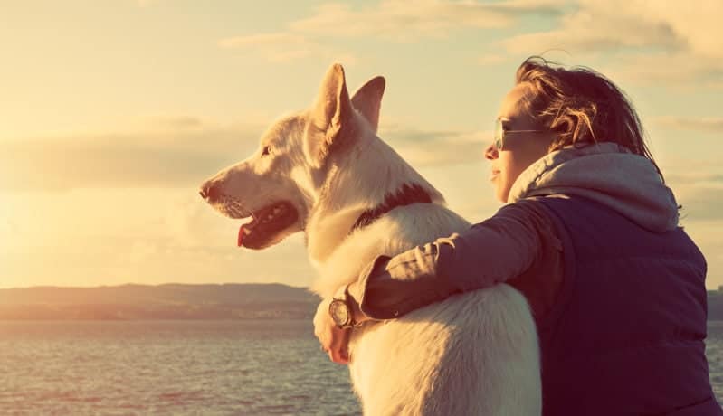 Una chica joven que abraza a su perro mientras ven al horizonte en la playa de Sitges